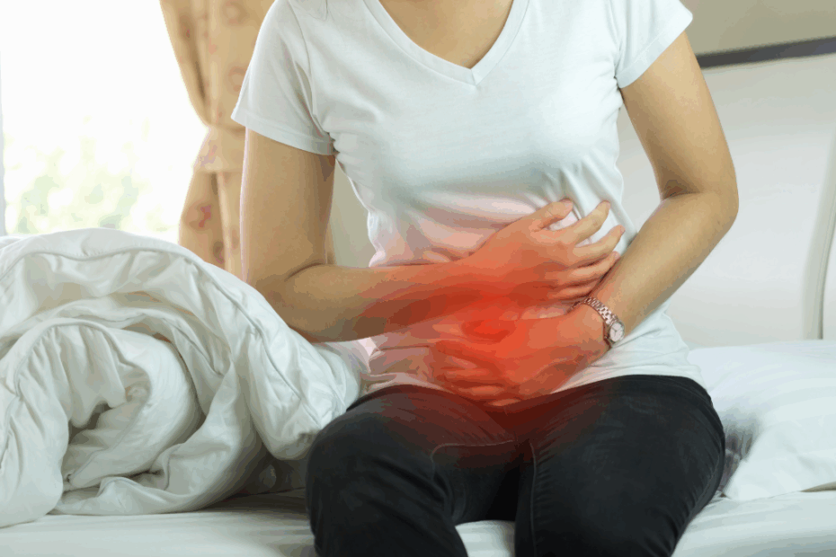 Mujer con dolor abdominal asociado a inflamación silenciosa, sentada en la cama y sujetándose el estómago.